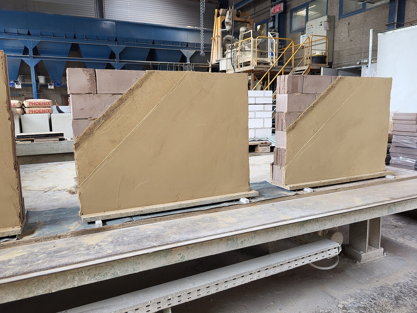 Große, rechteckige Betonfertigteile mit schrägen Kanten auf Transportgestell in Werkhalle.