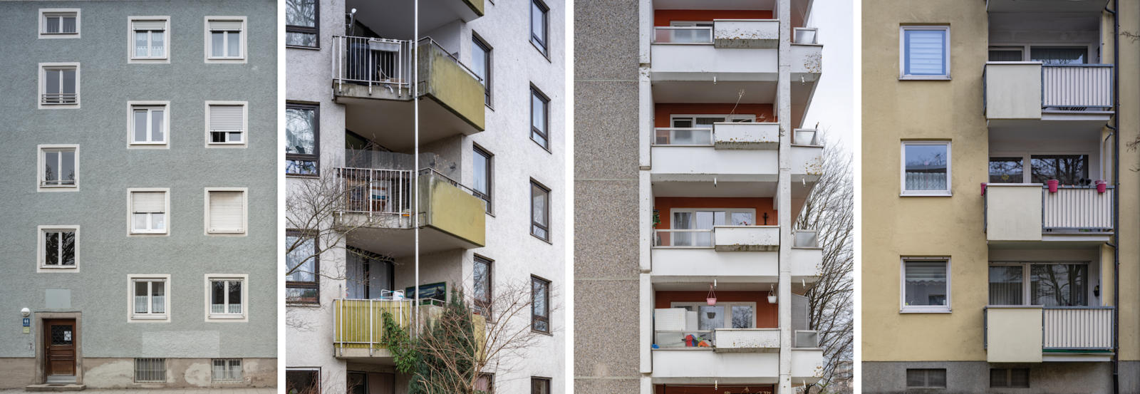 Drei Mehrfamilienhäuser mit Balkonen, verschiedene Farben: grau, beige und gelb, Winterszene mit kahlen Bäumen.