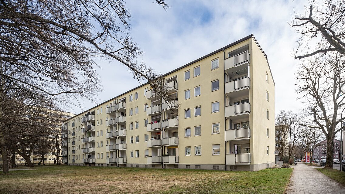 Fünfstöckiges Wohngebäude mit Balkonen in ruhiger Grünanlage, winterliche Bäume ohne Blätter.